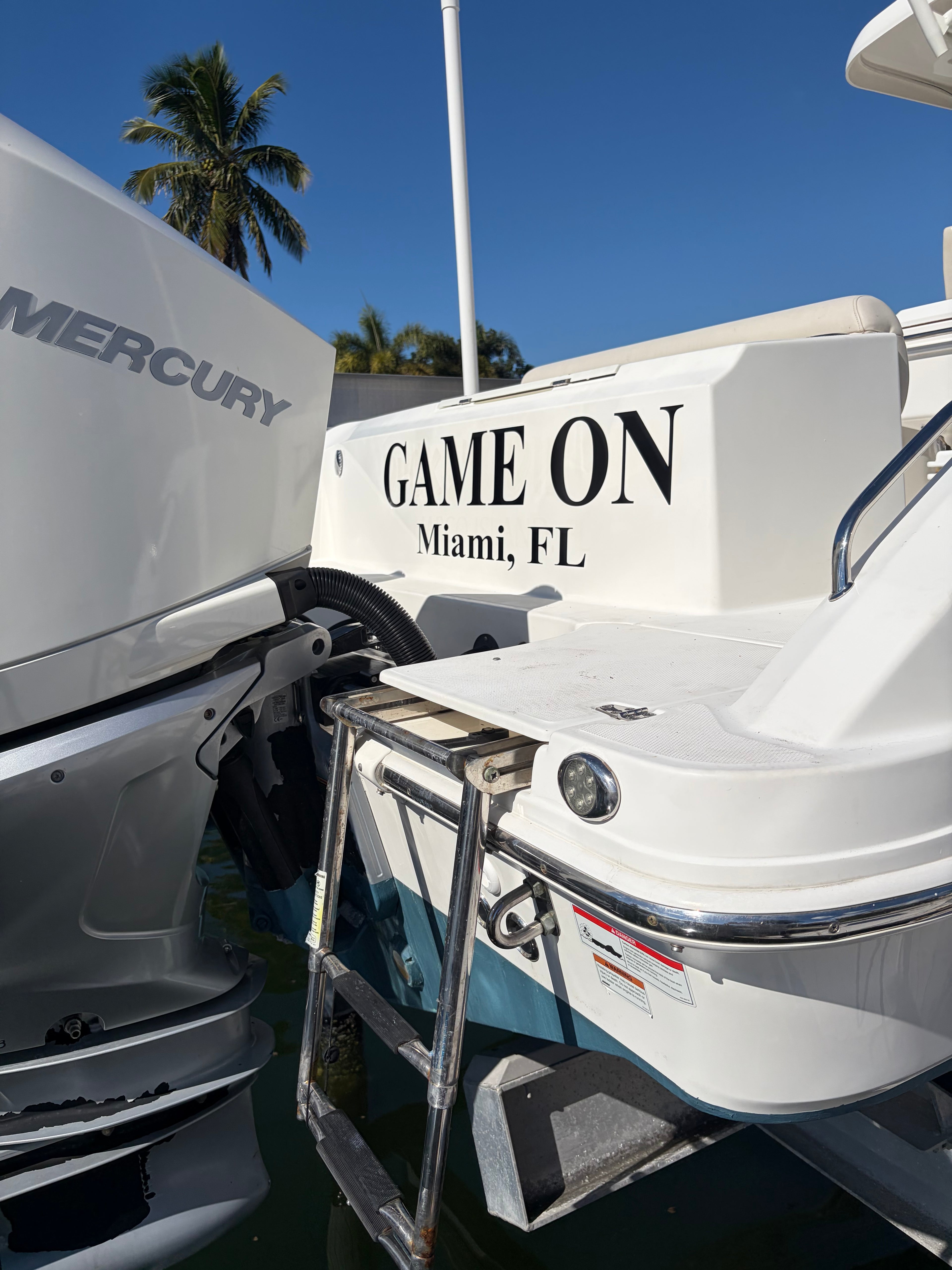 Boat with 'Game On Miami, FL' text next to a Mercury outboard motor on a clear day.