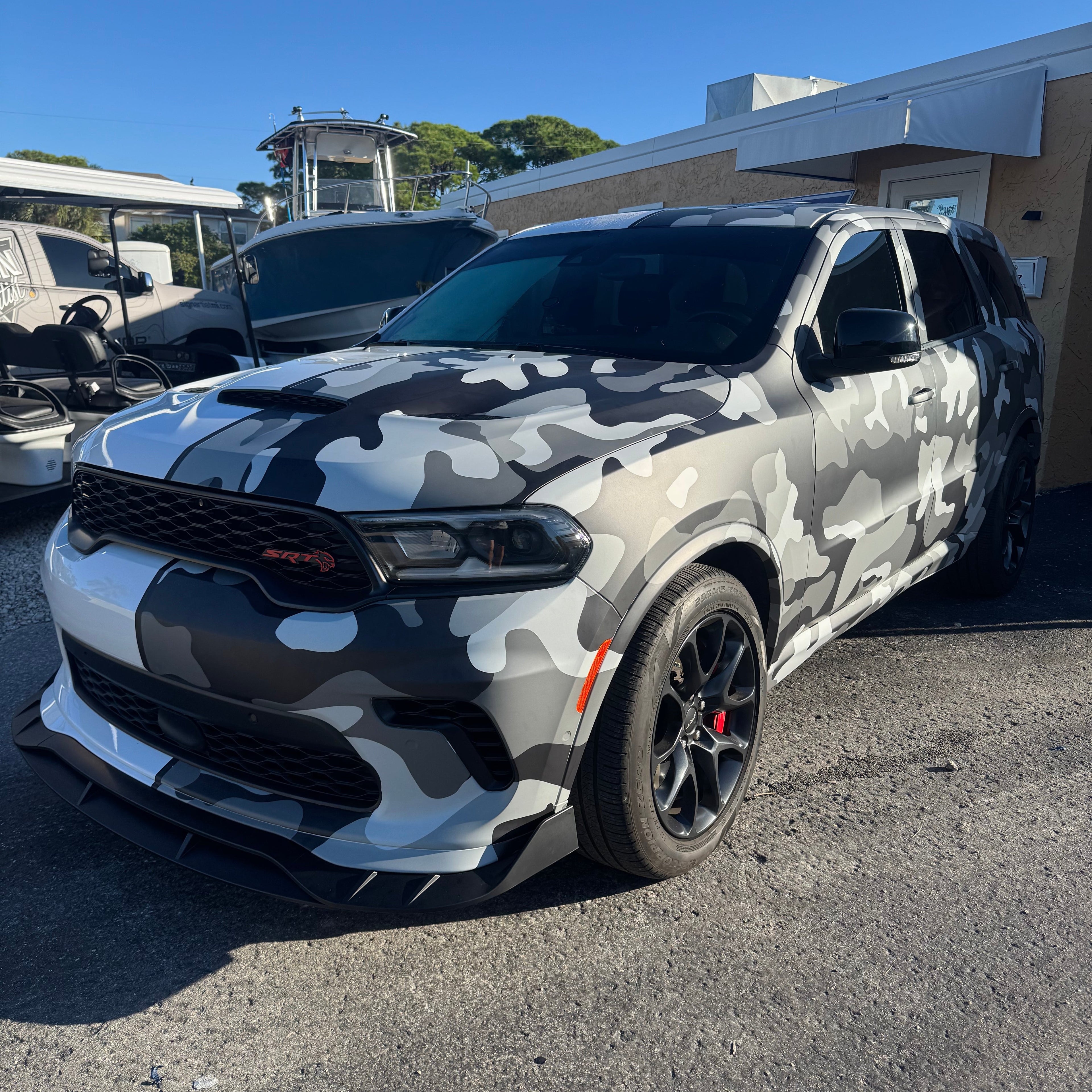Camouflage-patterned SUV parked in a lot with boats in the background