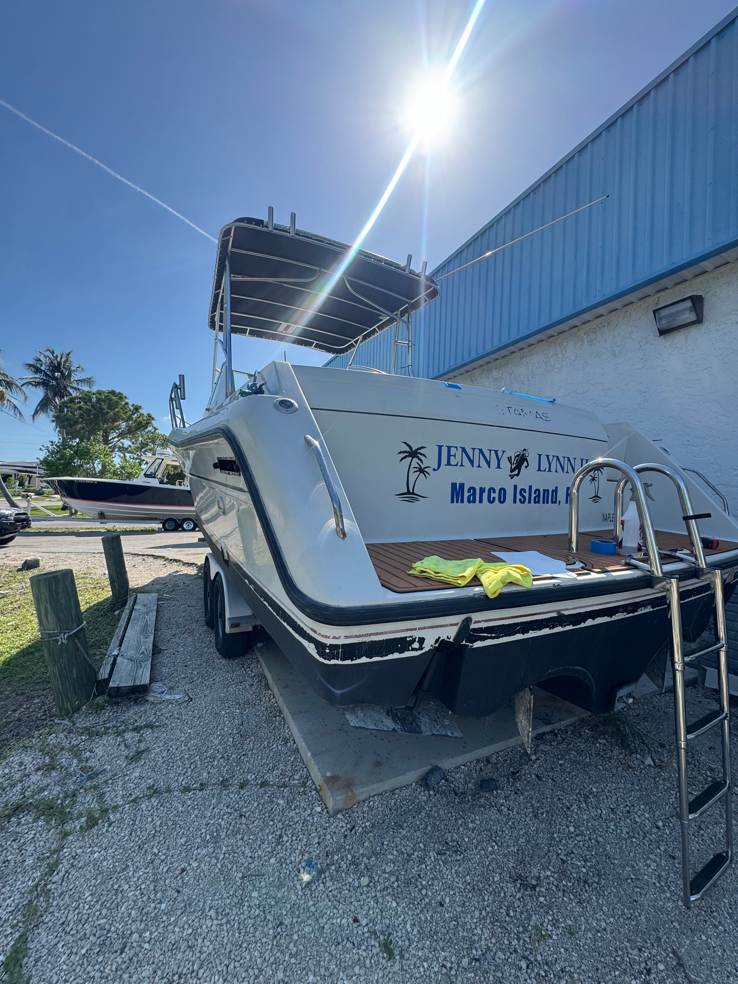 Marine trailer with a boat on a gravel surface under a clear blue sky.
