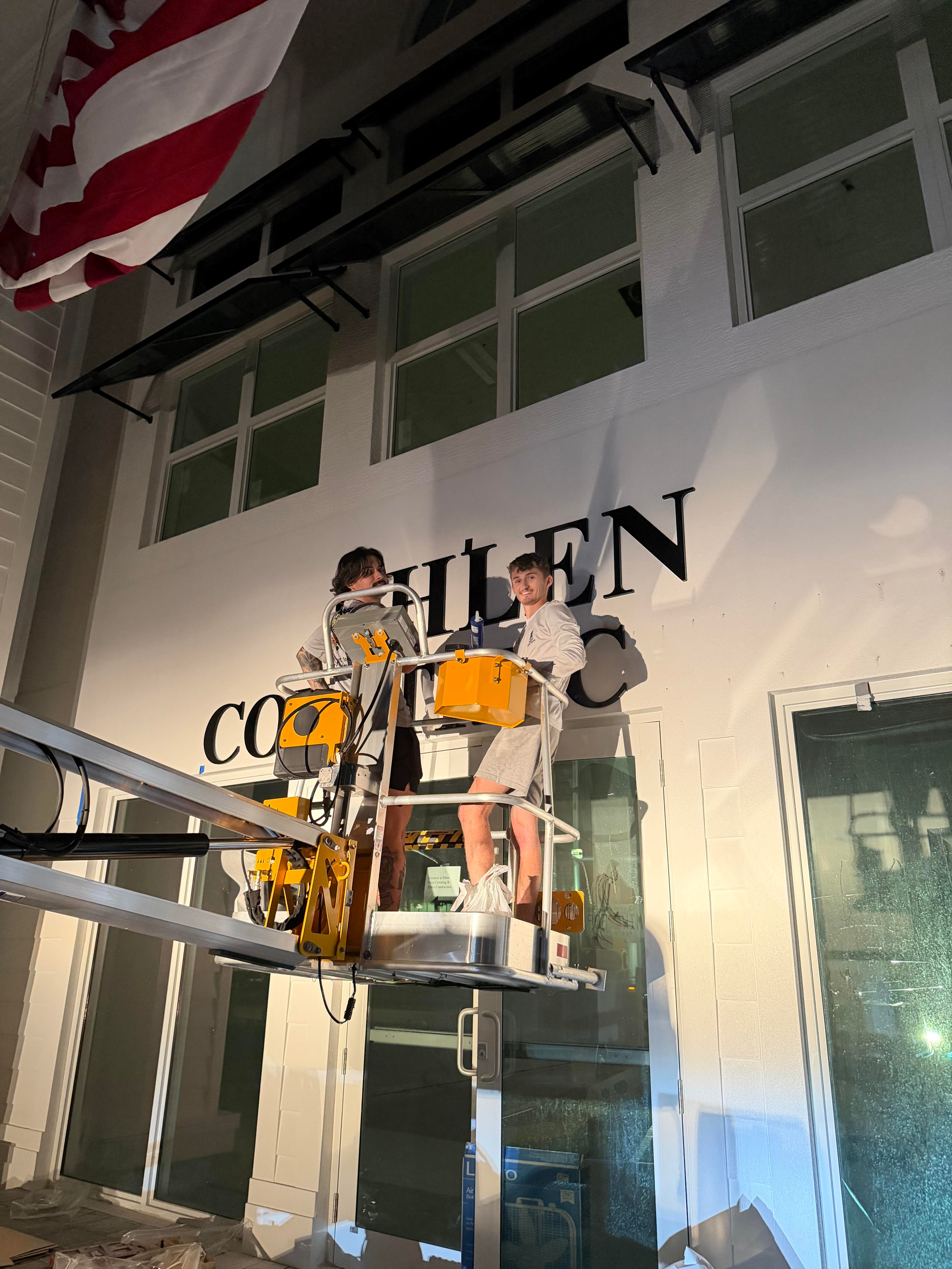 Two people on a ladder working on a building facade with 'COHEN' branding.